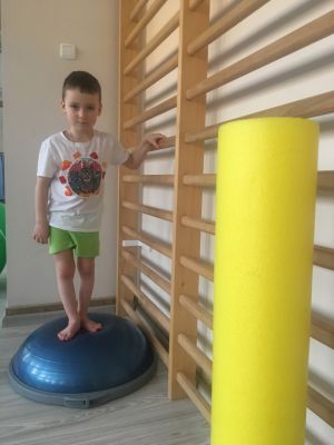Chłopiec ćwiczy równowagę na półkuli sensorycznej przy drabinkach